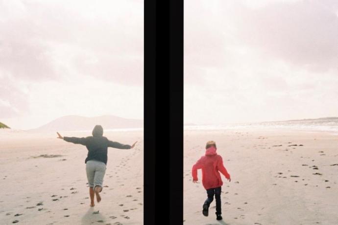 Two people running on the beach, one capturing the moment with a camera while enjoying the sunny day.