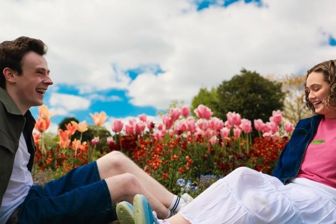A couple enjoys a moment on the grass, facing a beautiful field filled with blooming tulips.
