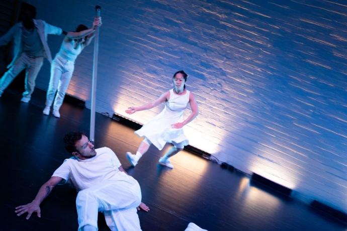 A man in white lies on the floor surrounded by other dancers in motion, showcasing a dynamic dance performance.