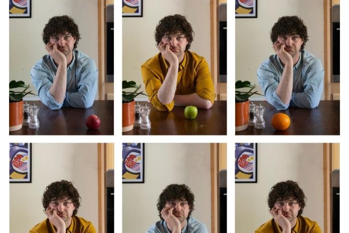 A man at a table with an array of colorful fruits, appearing deep in thought or reflection.