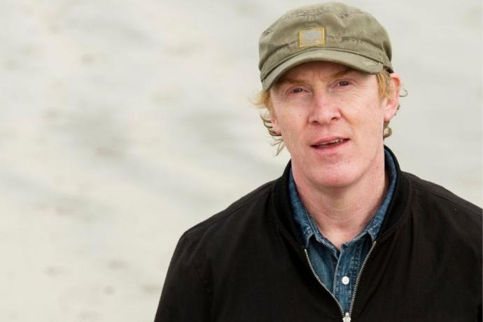a headshot of the artist in a hat and jacket.