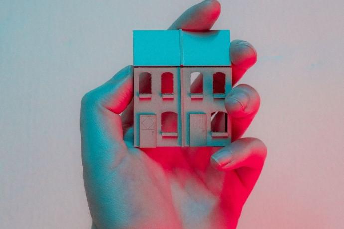  A person gently holds a small house in their hand, symbolizing care and ownership.
