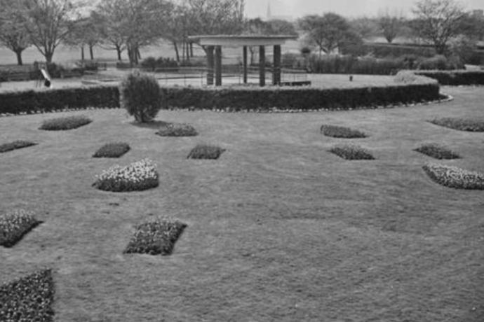 A black and white image showcasing a garden with a gazebo at its center, framed by various plants and trees.
