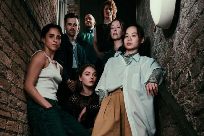 A group of people, including men and women in formal clothing, are standing together on a staircase. The background features a wall.