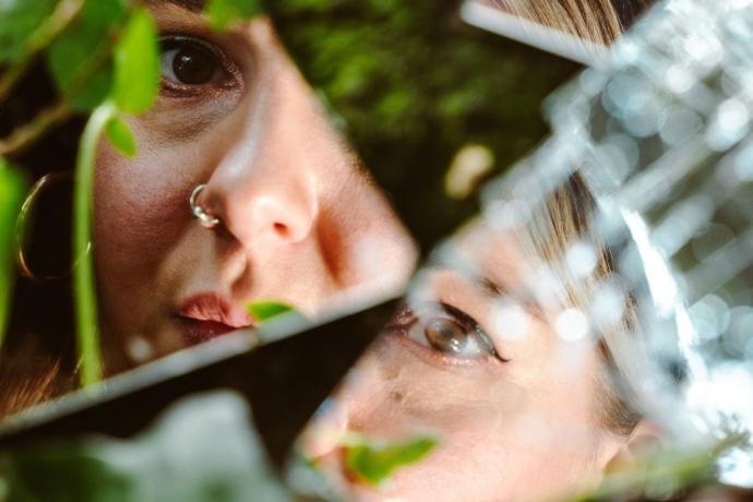 A womans face reflected in shattered glass scattered on top of grass.
