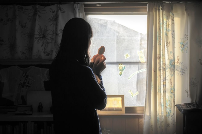 A woman gazes out a window holding an object 