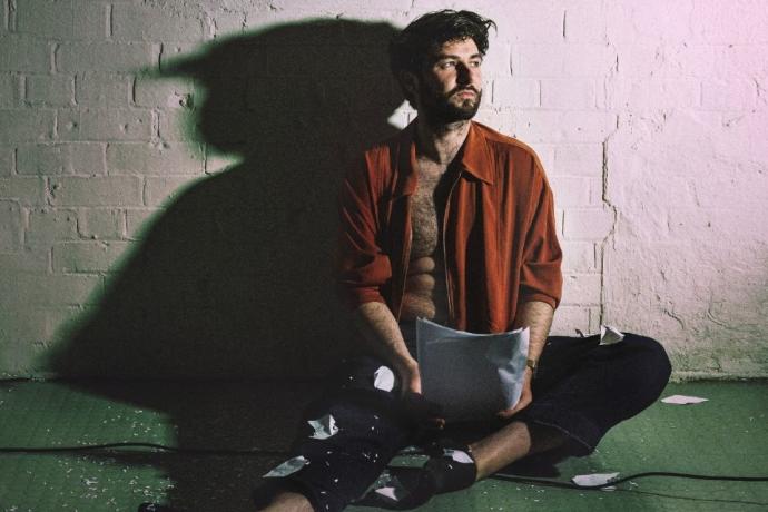 A man on the floor, holding a piece of paper but looking thoughtfully away from it.