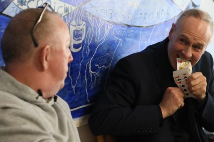 Two Men talk to each other in front of a blue wall