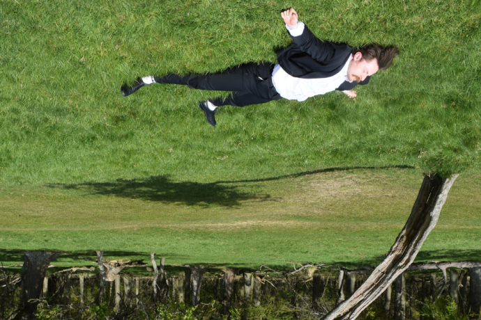 A performer appears to float sideways above a grassy landscape, with the image turned upside down.