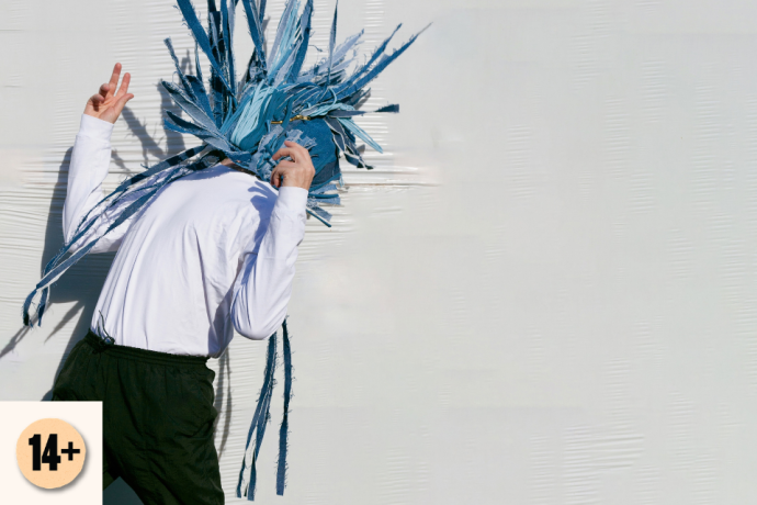 A performer with a blue shredded headpiece bends forward against a pale textured wall. Visible symbol: 14+.