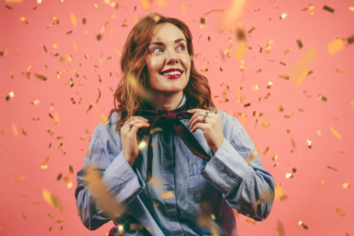 Image of a smiling  woman in front of a peach background with confetti floatting