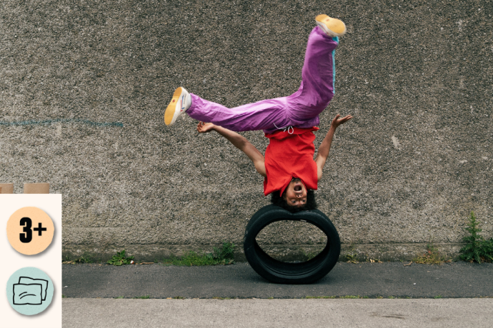 A performer in a red top and purple trousers balances upside down on a tyre against a concrete wall, with one foot kicked high in the air. Access and audience icons shown: 3+ and Relaxed Performance.