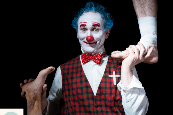 A smiling clown with blue hair and a plaid vest holding up two bare human feet against a black background. Visible access symbol:  Home Ground