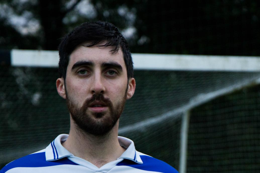 A head and shoulders shot of a man in a jersey standing in front of a goal post