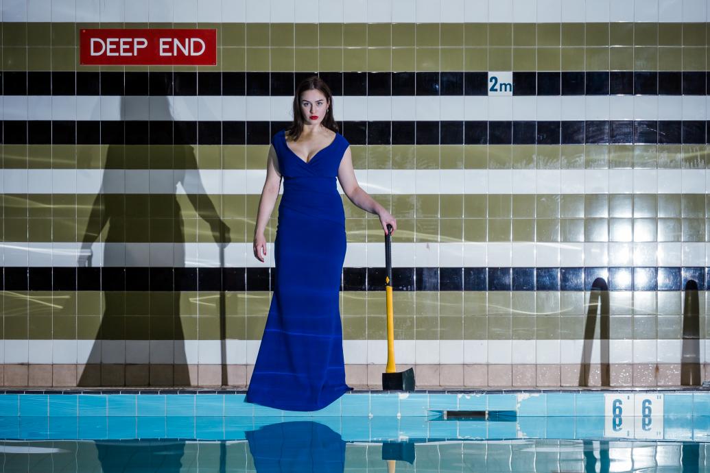 Woman standing at deep end of a pool, with an axe in hand