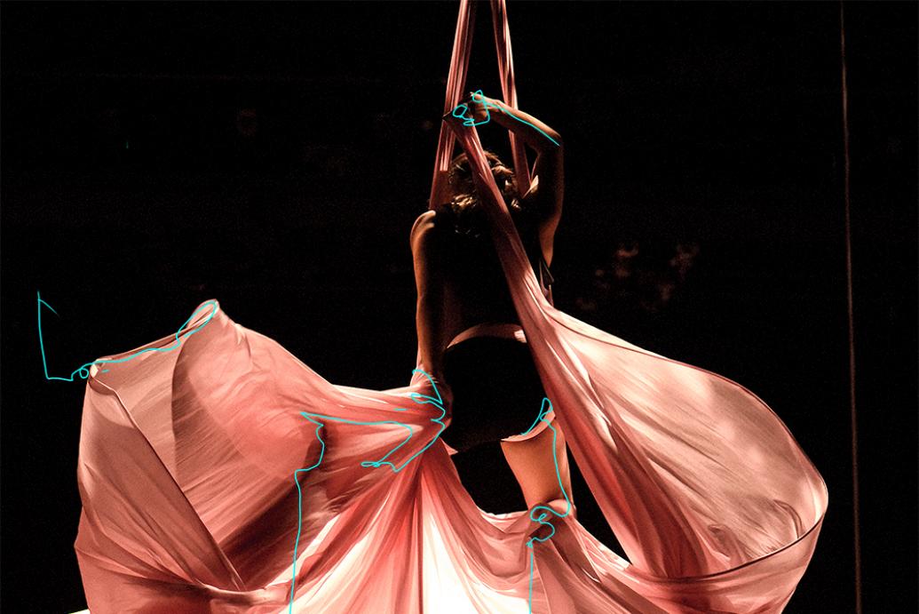 Sorry Gold, a woman hangs from an aerial silk with pink fabric billowing below her