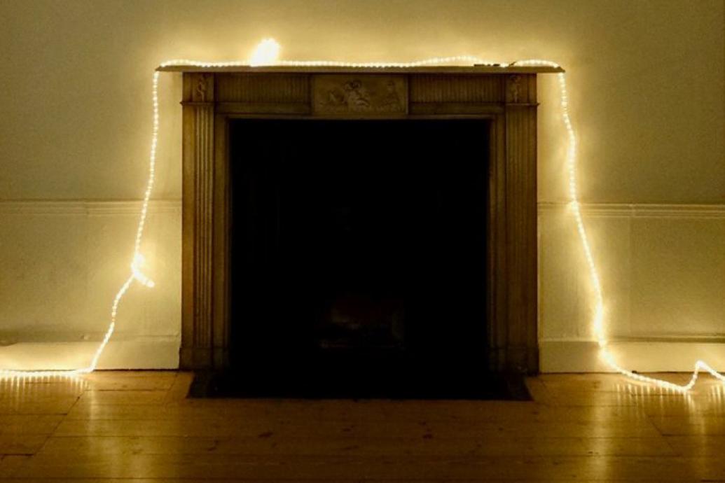 A dark fireplace is draped with a line of fairy lights that continues across the floor on either side of it in a beige room with wood floors