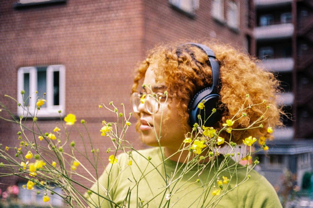 Woman with headphones by a yellow flowered bush