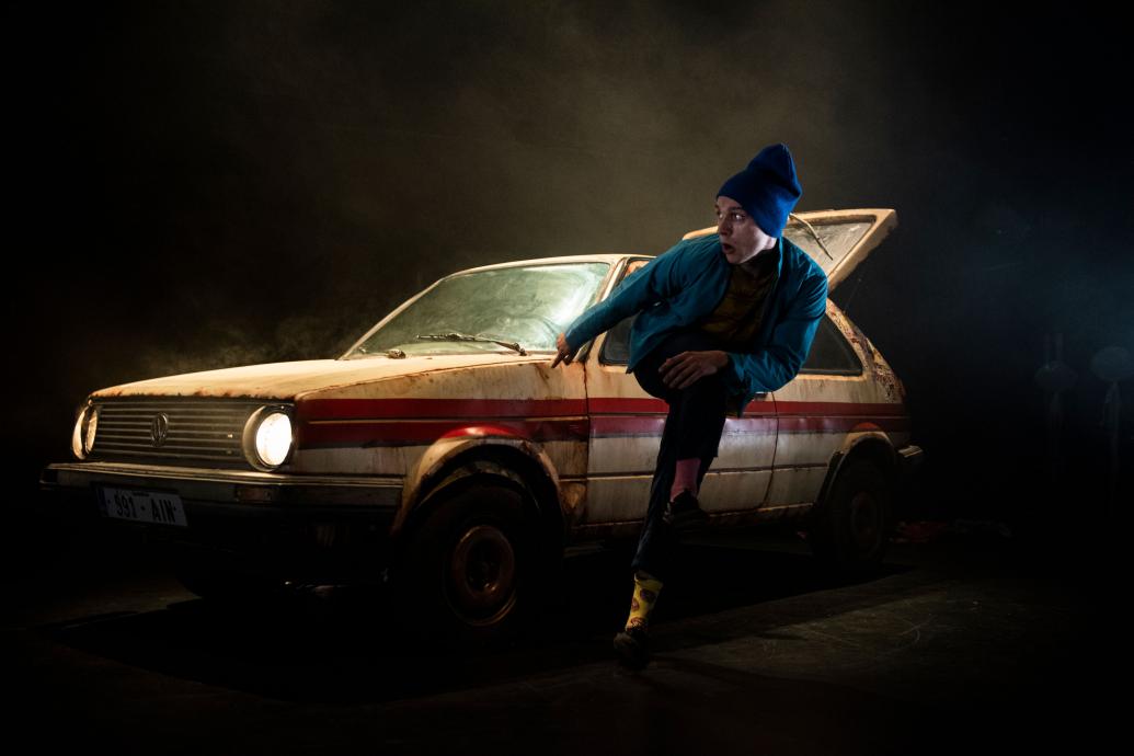 Young man dancing in front of a car with a dark background