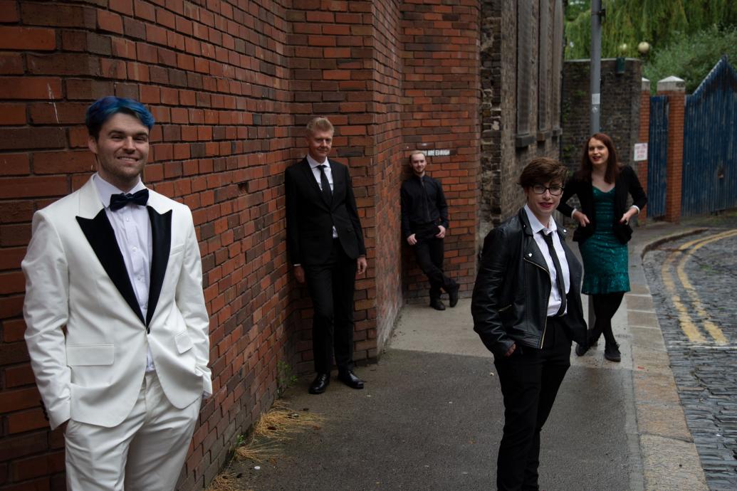 5 well dressed people stand along a red brick wall