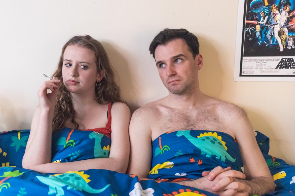 Image of a young woman smoking in bed next to a young man