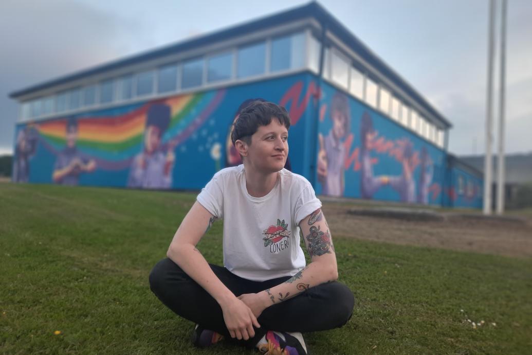 Portrait of artist Emmalene Blake sitting on the grass in front of her mural