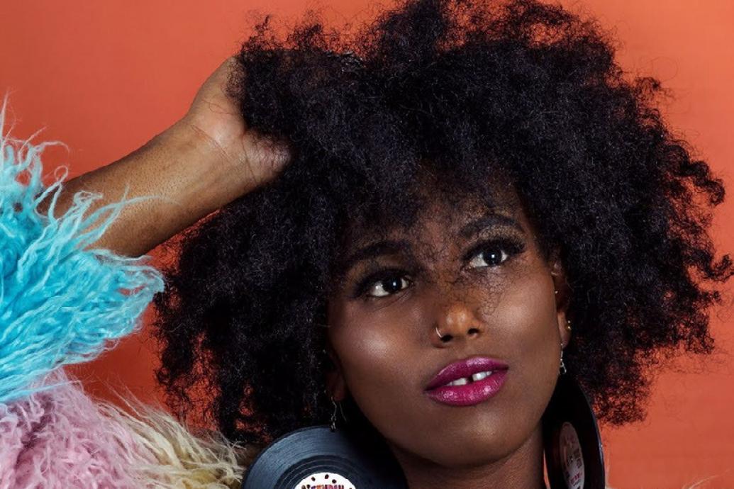 Image of Fehdah against an orange backdrop with her hand in her hair