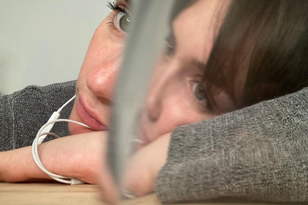 A woman listening to headphones obscured by a glass