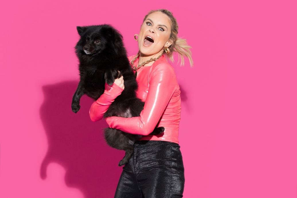 Image of Joanne holding a black dog against a pink background