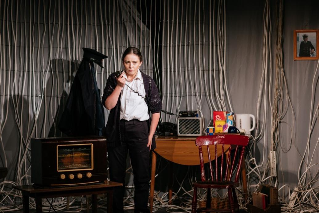 Actor on stage with radio in hand, listening intently