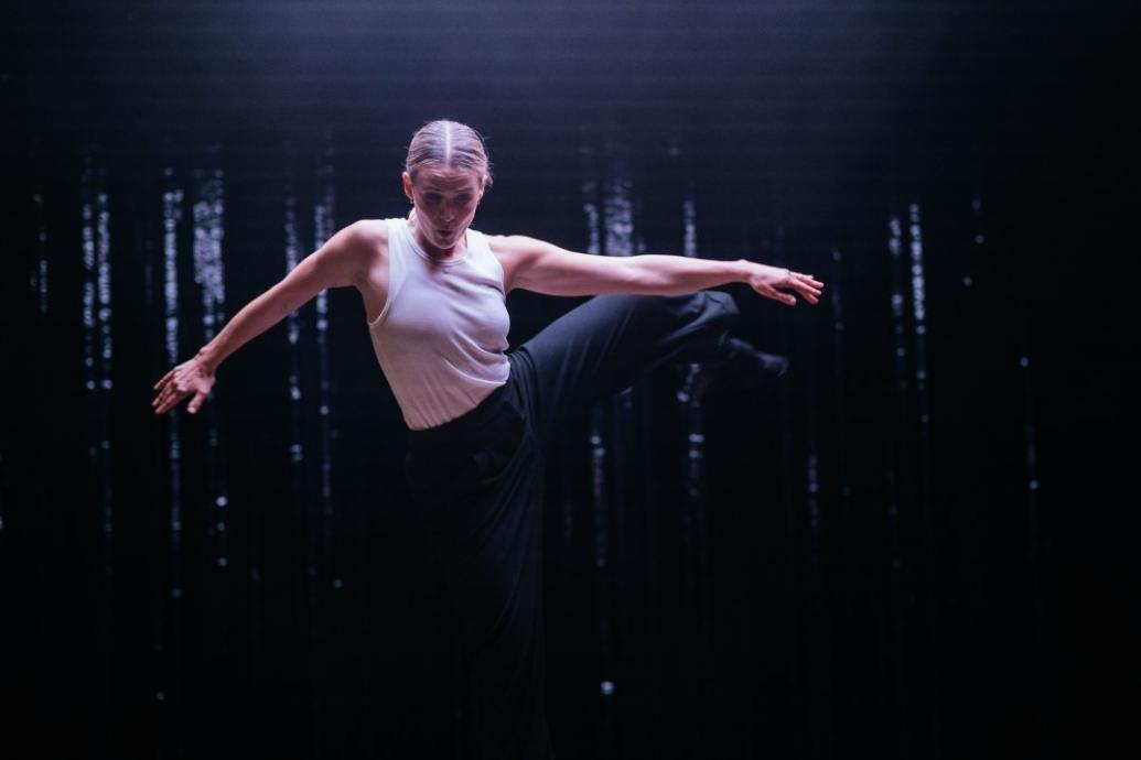 Performer Sibeal Davitt dancing on a blacked out stage lit by a single spotlight