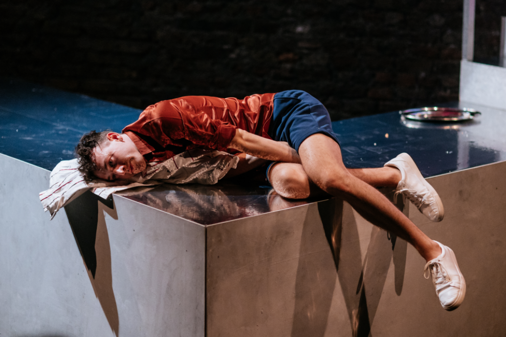 A performer lying across a corner of the stage, asleep