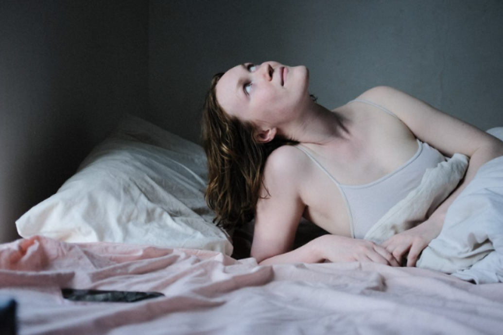 A young woman lying in bed propped up on an elbow looking up at the ceiling