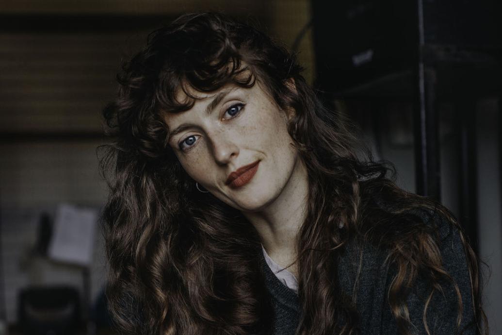 A white woman with long brown hair and red lipstick with her head tilted to the side looking straight at camera