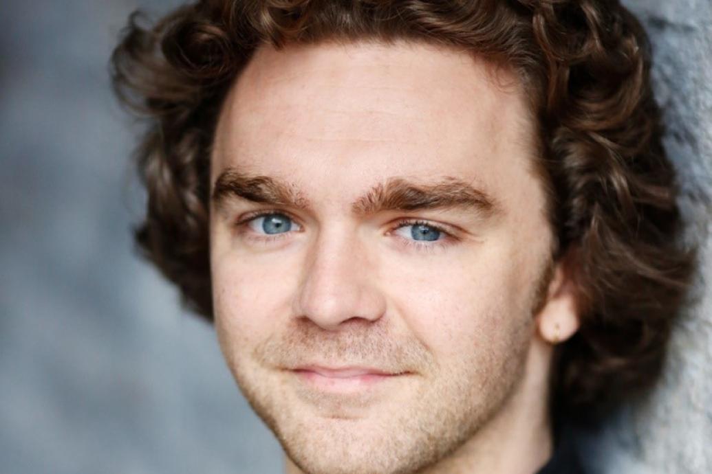 Headshot of a white man with brown curly hair smiling directly to camera