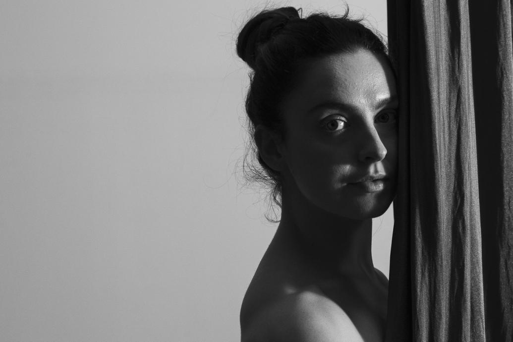 Black and white image of a woman looking to camera side on  holding draped material