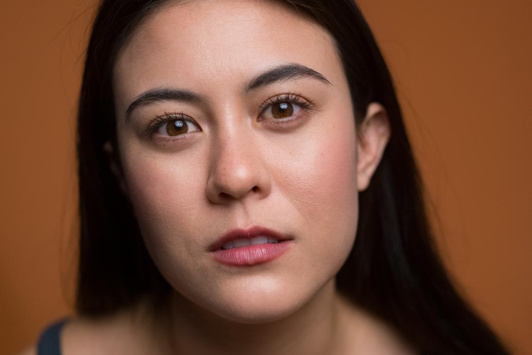 A headshot of a woman wearing a black top against a brown background.