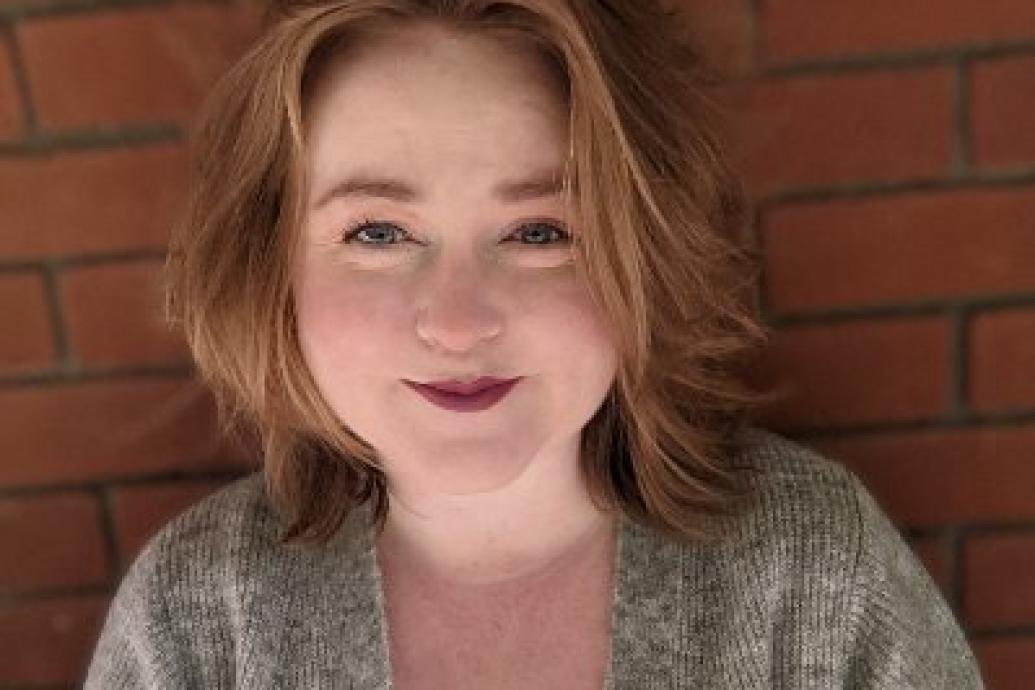 A headshot of a person standing against a red brick wall. 