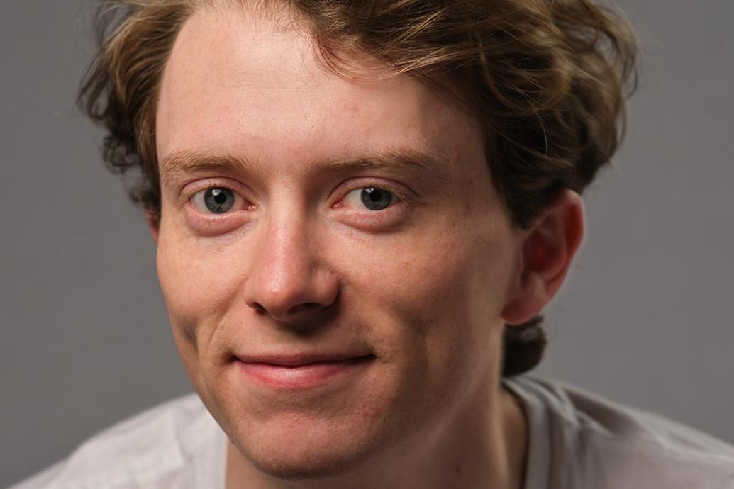 A headshot of a person wearing a gray top against a gray background.