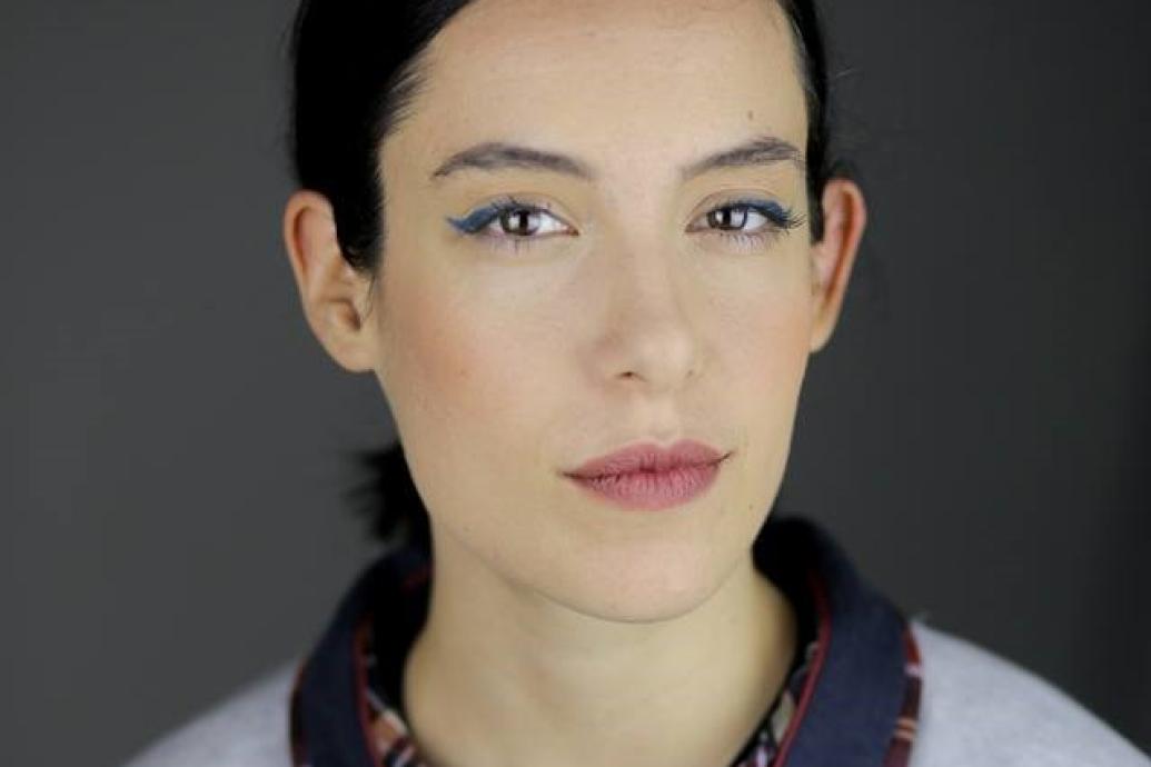 A headshot of a person wearing a gray top against a gray background.