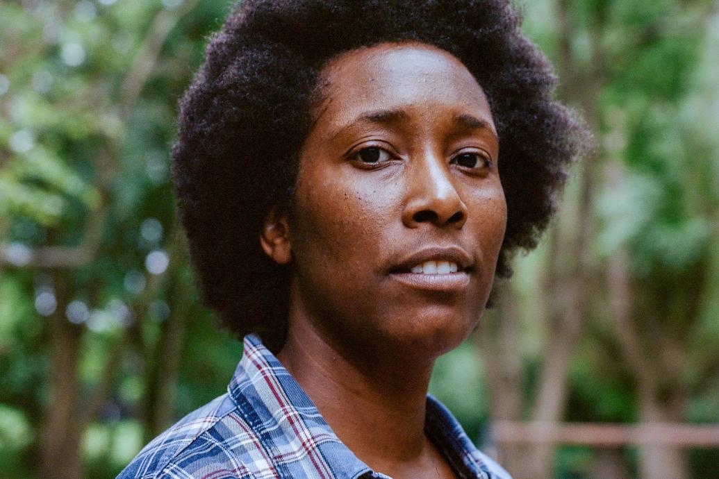 A headshot of a person wearing a check shirt with trees behind. 