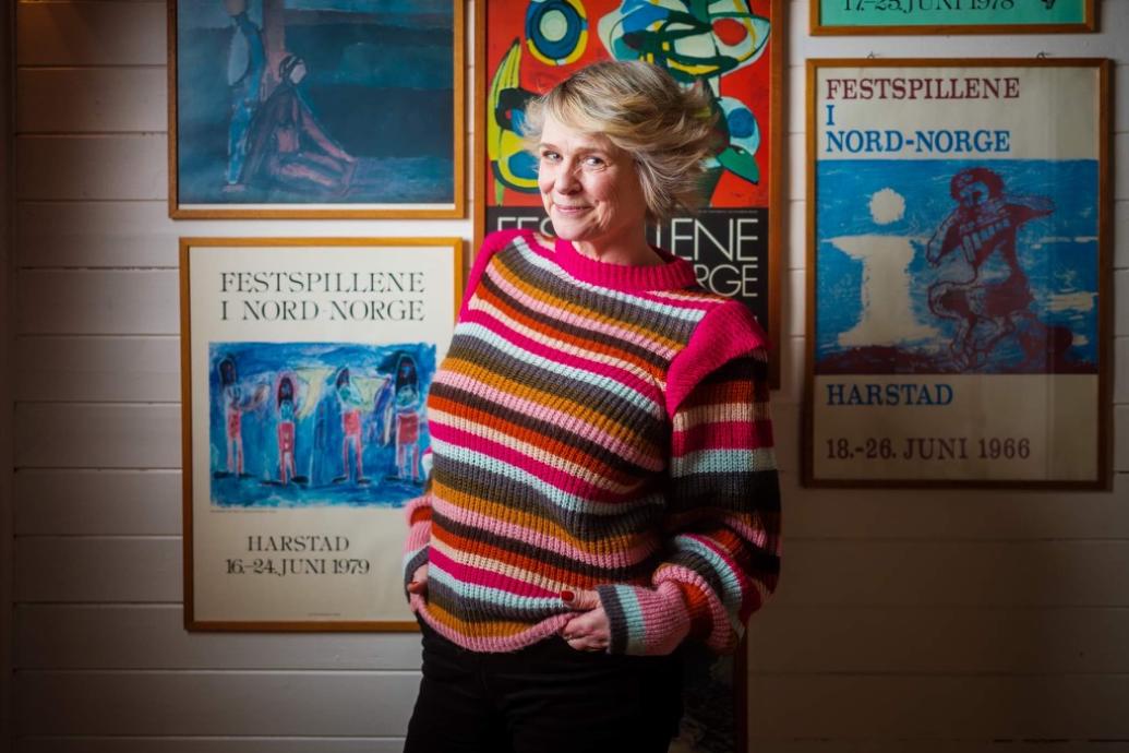 A person wears a colourful pullover against a wall of theatre posters