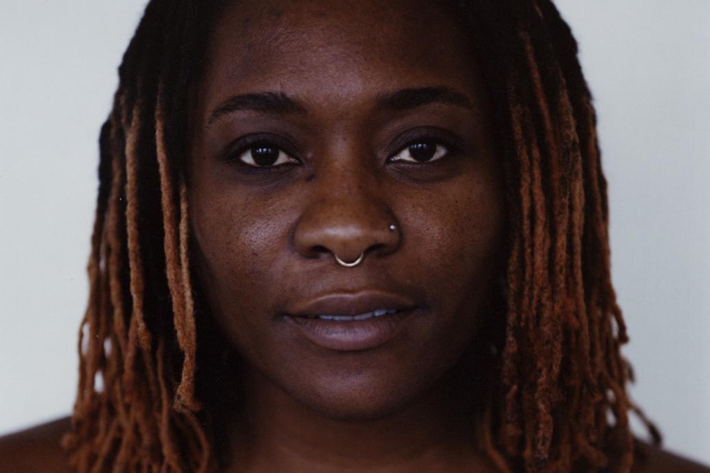 A headshot of a person wearing a dark top against a gray background