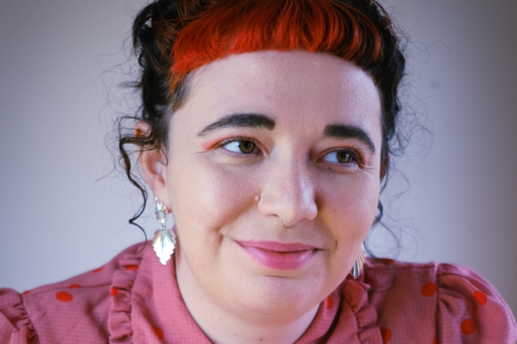 A close up headshot of a person wearing a red top