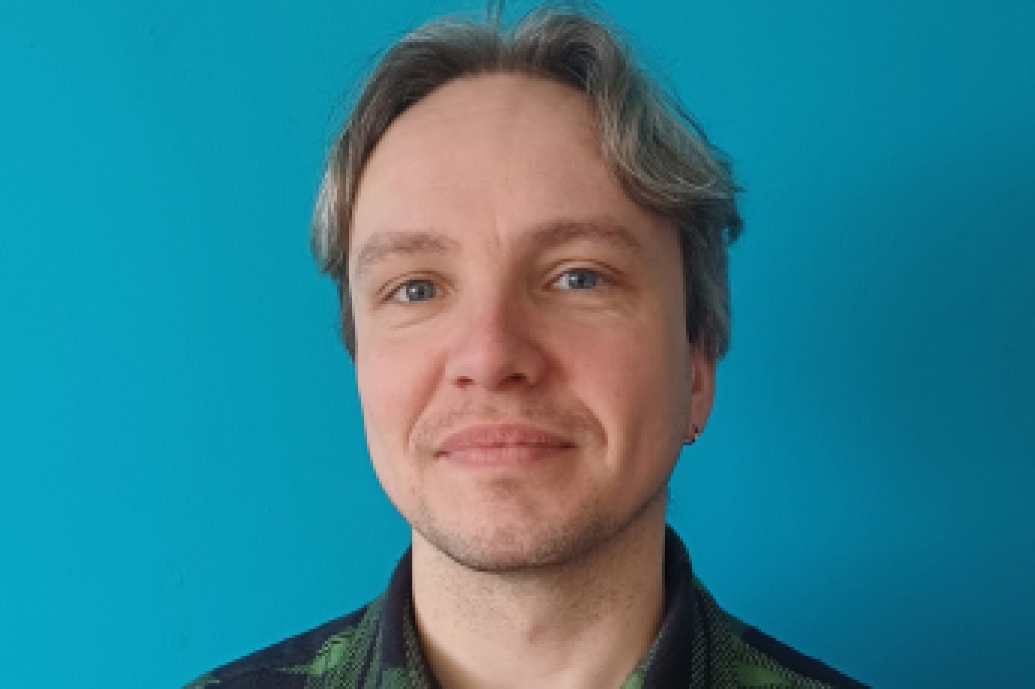 Man in check shirt standing against blue wall