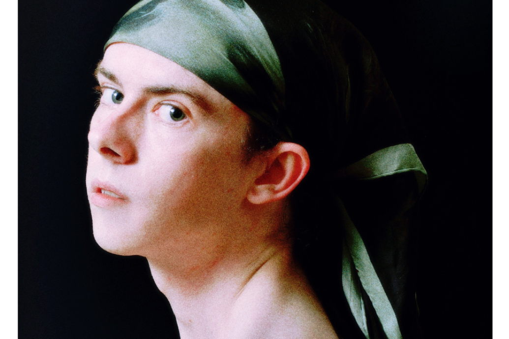 A person with a serene expression gazes to the side, wearing a green silk headscarf against a dark background, evoking a classic, timeless feel.