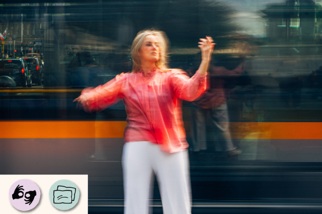 A performer in a coral top stands in front of a moving tram, blurred by motion. Visible access symbols: ISL and Relaxed Performance.