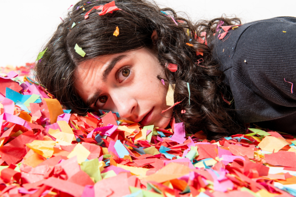 A close-up of a person lying in colourful confetti, looking toward the camera.