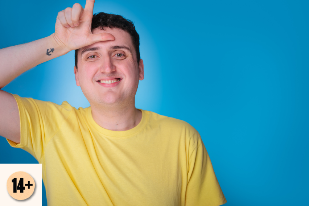A smiling man in a yellow T-shirt makes an L shape with his hand against a bright blue studio background. Visible access symbol: 14+.