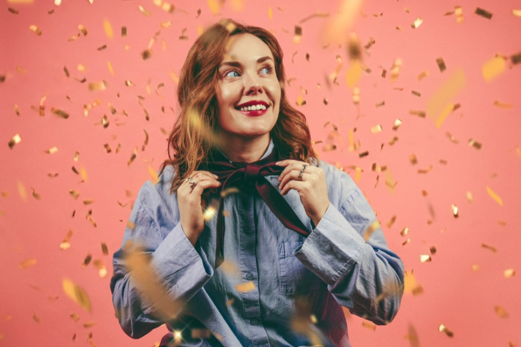 Image of a smiling  woman in front of a peach background with confetti floatting